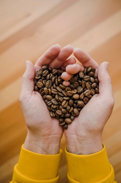 Foto vista superiore del barista che tiene i chicchi di caffè in mani a forma di cuore