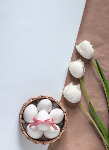 Top view of a basket with white Easter eggs and white tulips on a white background