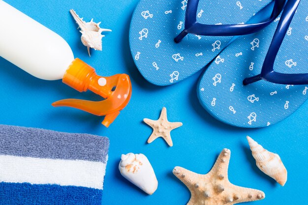 Top view of Beach flat lay accessories. sunscreen bottle with seashells, starfish, towel and flip-flop on Colored background with copy space.