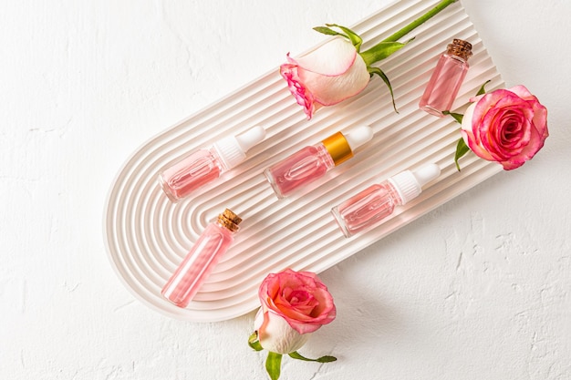 Top view of a beautiful composition of cosmetic bottles with a product of rose petals and buds of live roses on a white plaster tray arch Flat lay