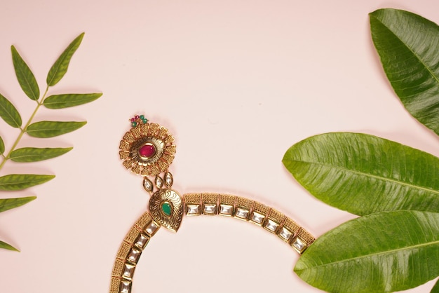 Top view of a beautiful necklace on a pink surface decorated with green leaves