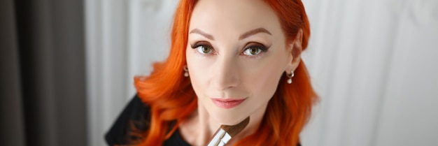 Top view of beautiful red haired makeup artist posing in beauty salon holding professional