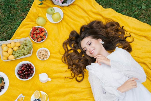 Top view of a beautiful romantic woman in a dress lying on the green grass on a yellow blanket