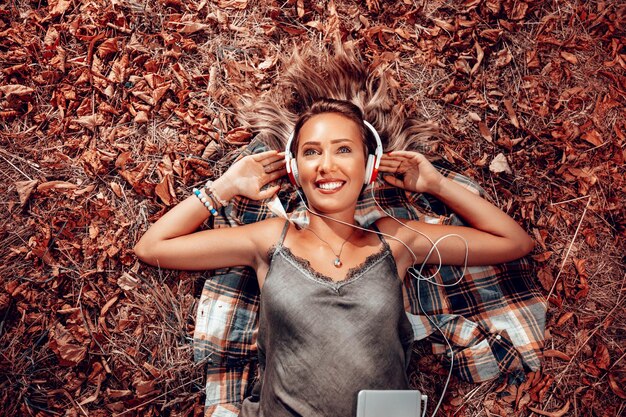 Photo top view of a beautiful smiling girl lying on the falls leaves and listening music.