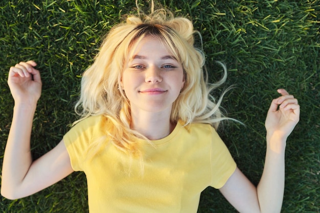 Top view of a beautiful teenage blonde lying on the green grass