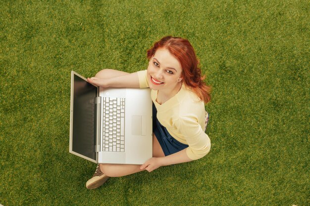 Foto vista dall'alto della bella donna seduta sull'erba verde con un computer portatile signora felice con labbra rosse guardando la fotocamera turismo o concetti freelance