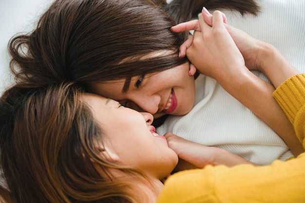 Top view of beautiful young asian women lesbian happy couple hugging and smiling while lying together in bed under blanket at home. Funny women after wake up. Lesbian couple together indoors concept.