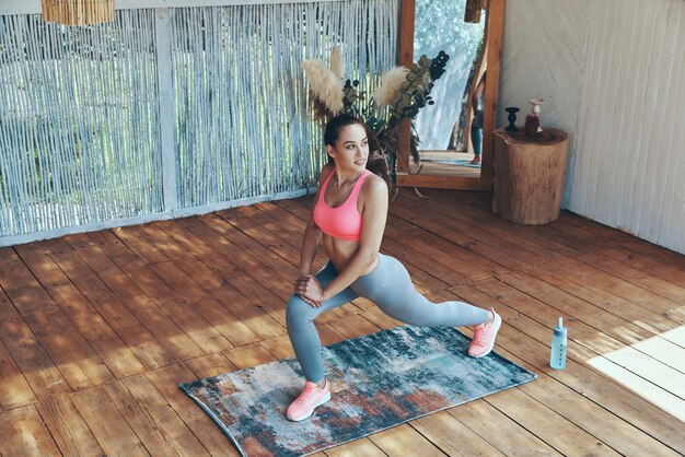 Top view of beautiful young woman in sports clothing doing stretching exercises on patio