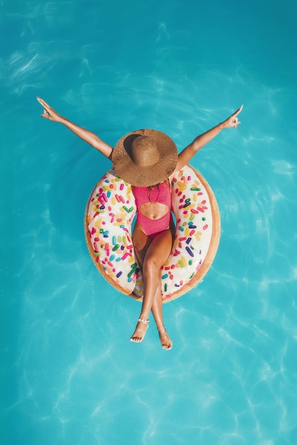 Top view of a beautiful young woman in swimming pool swims on inflatable ring donut and has fun on vacation.