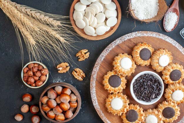 top view biscuits with chocolate and dark chocolate on wood board bowl with white chocolate rounds and hazelnuts on table