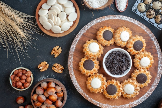 top view biscuits with chocolate and dark chocolate on wood board bowl with white chocolate rounds nuts on table