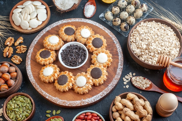 top view biscuits with chocolate and dark chocolate on wood board bowls with nuts oats candies quail eggs in viol wooden spoon honey jar on table