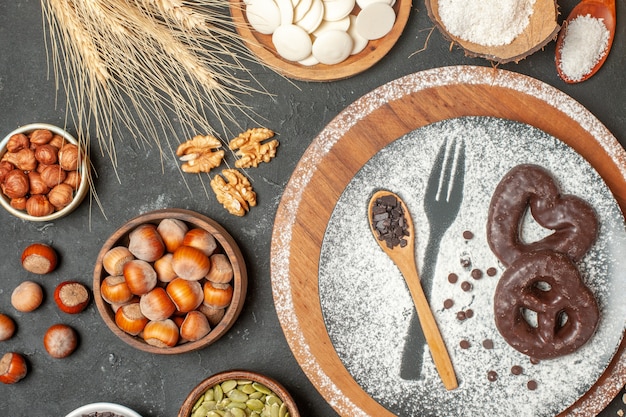 top view biscuits with chocolate fork imprint with icing sugar wooden spoon on plate white chocolate rounds coconut powder hazelnuts in bowls on table