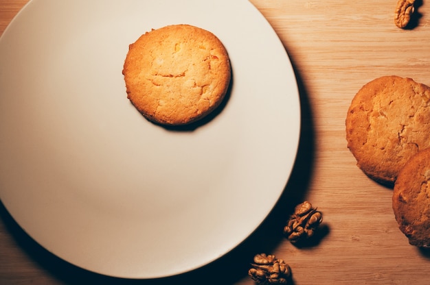 Top view of biscuits with wallnuts, on a white plate and wooden table