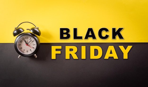 Photo top view of black alarm clock and the text on yellow and black background shopping concept boxing day and black friday composition