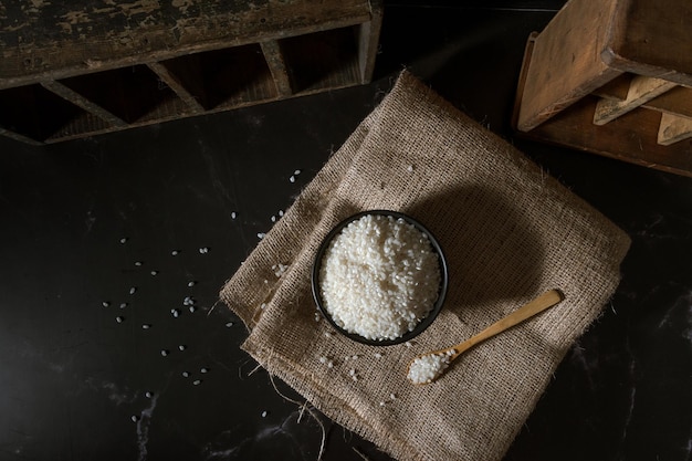 Top view of black bowl and wooden spoon with raw white yamani rice