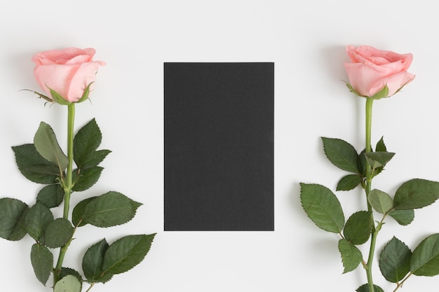 Top view of a black card mockup with pink roses on a white table