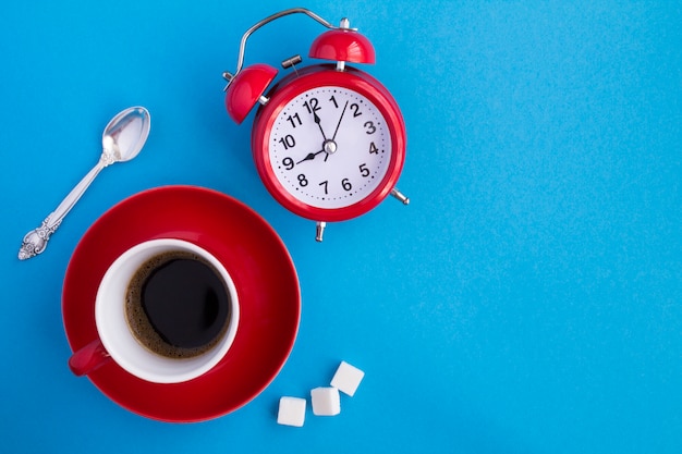 Vista dall'alto di caffè nero nella tazza rossa e sveglia rossa sulla superficie blu