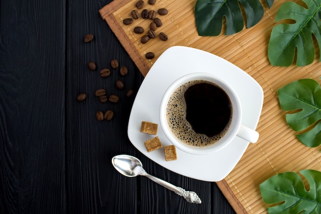 Top view of black coffee in the white cup on the tropical background