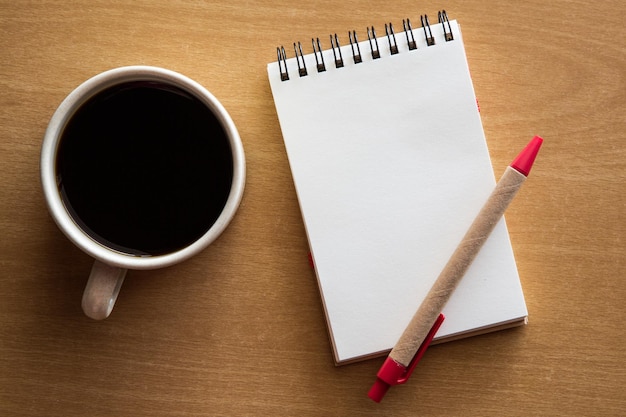 Top view of black coffee with notepad and pen on wooden table