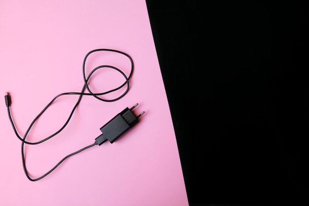 Photo top view of black color usb mobile charger on pink and black background with copyspace