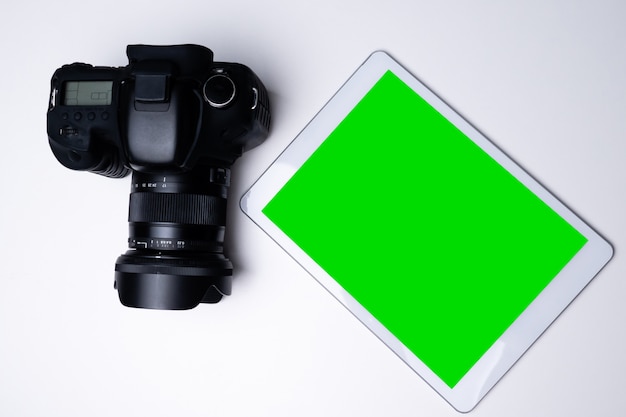 Photo top view of a black digital camera and a blank screen tablet on a table.