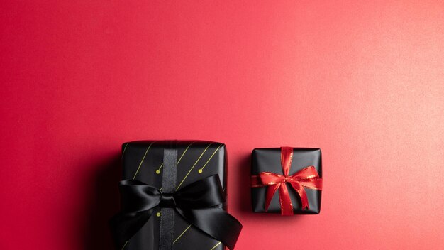 Top view of black gift box with red and black ribbons isolated on red background