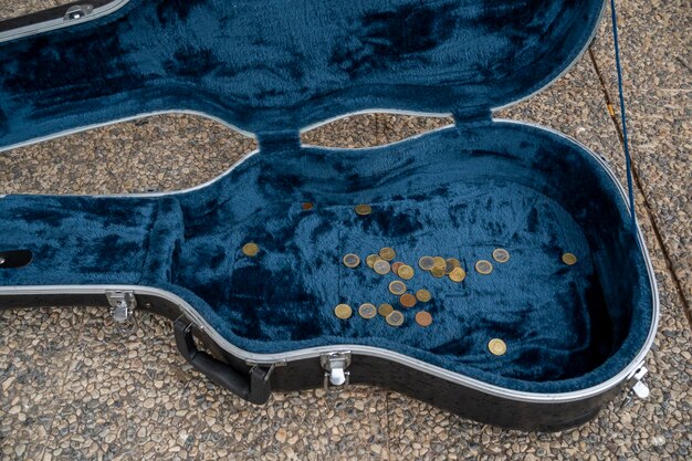 Photo top view of black opened guitar case with golden coins placed on asphalt pavement during live concert of street performer