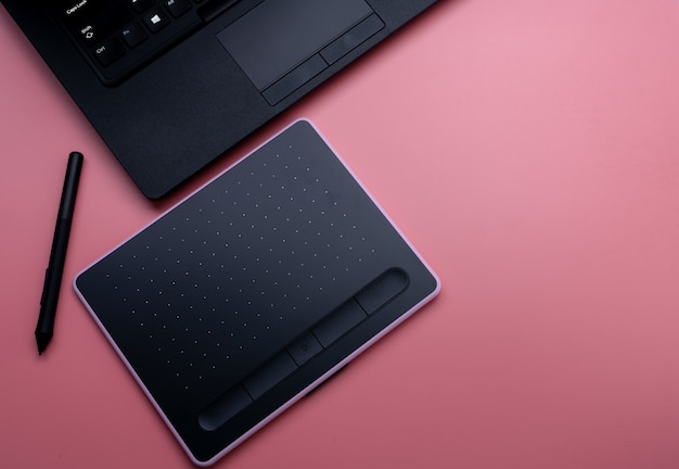 Top view of black pen mouse, digital tablet, and laptop for graphic design work on pink background. Above view of pen graphic tablet. Gadget for graphic designer. Bluetooth and wireless device.