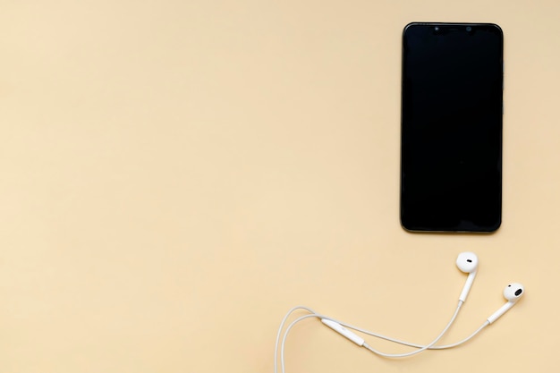 Top view of black smartphone with blank screen and wire headphones mobile phone as music gadgets on beige background top view copy space