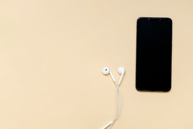 Top view of black smartphone with blank screen and wire\
headphones mobile phone as music gadgets on beige background top\
view copy space