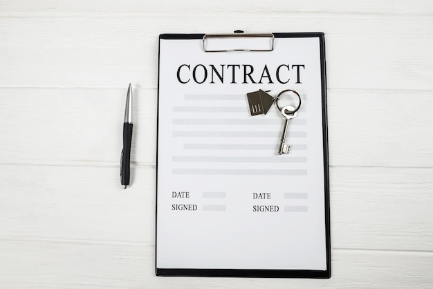 Top view of blank house lease or purchase agreement form with clipboard and key on white table