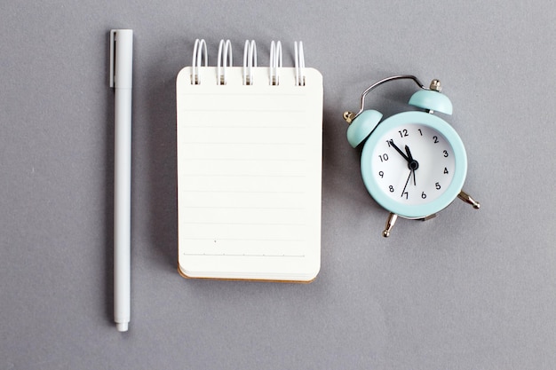 Top view of blank note paper with pen and alarm clock on gray background