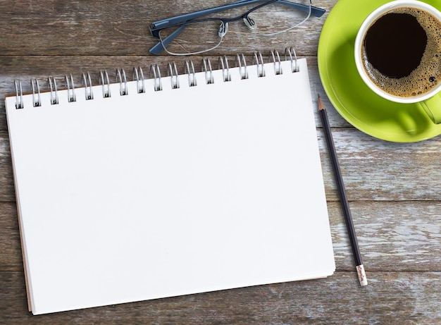 Top view blank notebookglasses and coffee on wood table background on office desk