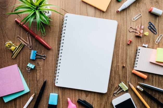 Top view of blank notepad and office supplies on wood background