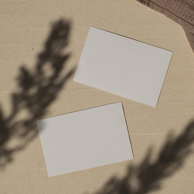 Foto vista dall'alto di fogli di carta bianca con mockup copia spazio in fiori ombre di luce solare su sfondo beige flatlay estetico modello di carta di invito matrimonio elegante minimalista
