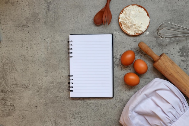 Photo top view of blank recipe notes with chef hat and cooking ingredients on grey rustic background