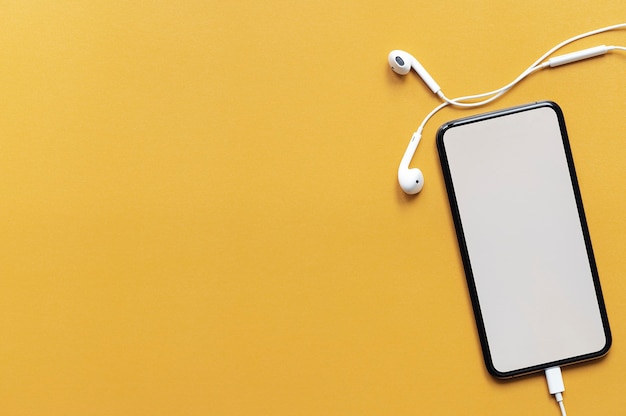 Top view blank screen smartphone with headset on yellow background.