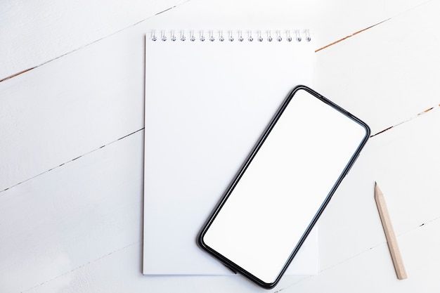 Photo top view of blank smartphone with white screen on paper notepad