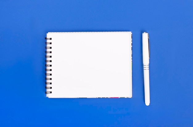 Top view of blank spiral notepad with pen isolated on blue background for mockup Minimal design copy space