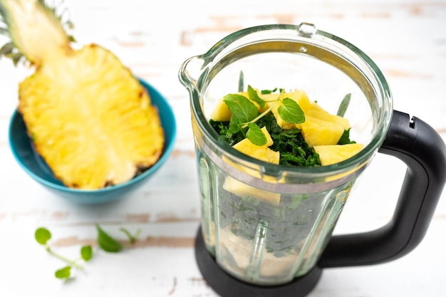 Top view of blender with avocado peaces and pinapple on white background