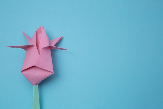 Foto vista dall'alto di uno sfondo blu con un tulipano rosa origami a sinistra. modello banner