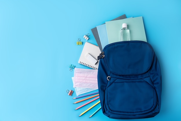 Top view of blue backpack with school stationery over blue table background, back to school design concept.