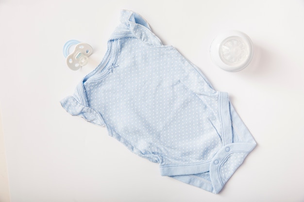 Photo top view of blue pacifier; baby onesie and milk bottle on white background