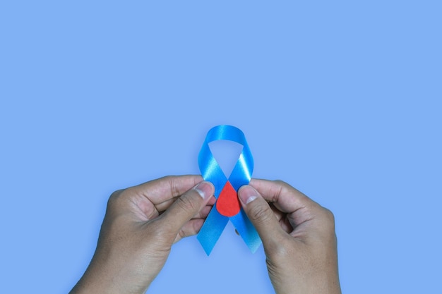 Top view blue ribbon awareness with red blood drop in man hands\
isolated on a blue background.