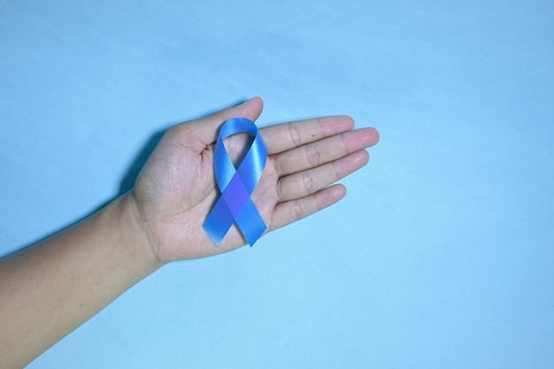 Top view blue ribbon awareness with red blood drop in man hands\
isolated on a blue background.