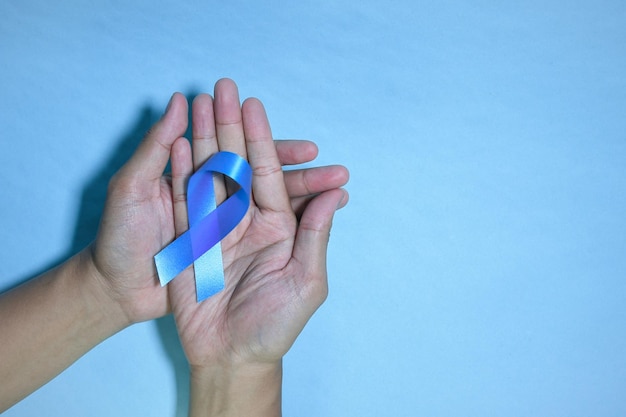 Top view blue ribbon awareness with red blood drop in man hands\
isolated on a blue background.