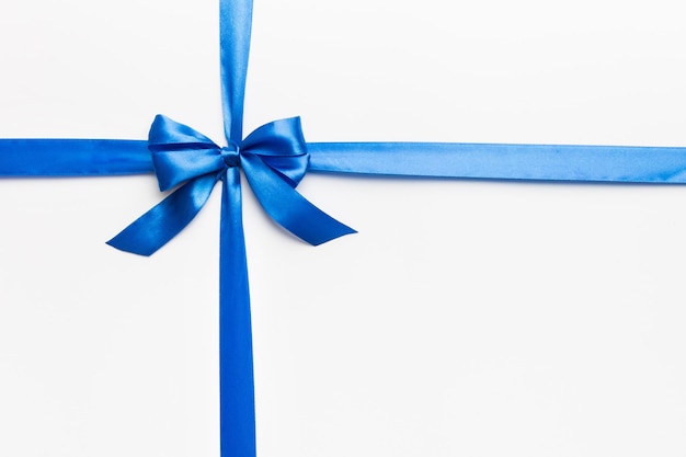 Photo top view of blue ribbon rolled and blue bow isolated on colored background flat lay with copy space