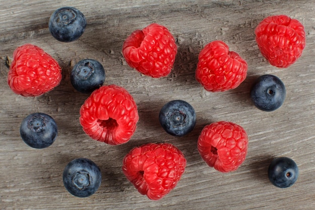 Top view on blueberries and raspberries spilled on gray wood desk.