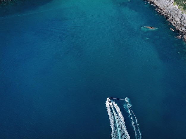 Top view of boat, leaving a white trail in blue deep water be
the rocky coastline; background. vessels.